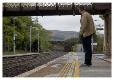 Side view of man standing at railroad station