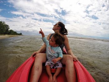 Mother with son kayaking in sea against sky