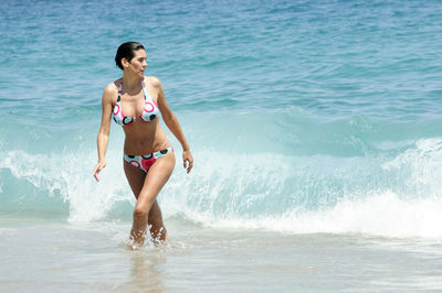 Seductive woman wearing bikini wading in sea during sunny day