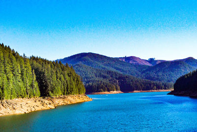 Scenic view of lake and mountains against clear blue sky