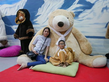 Portrait of mother and son sitting against large teddy bear