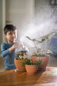 A boy sprays flowers in orange clay terracotta pots with a spray gun.