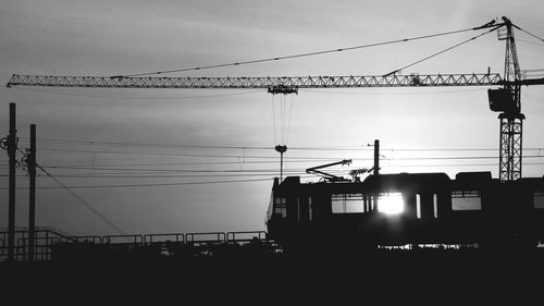 Silhouette electricity pylon by building against sky during sunset