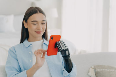 Young woman using mobile phone while sitting on bed at home