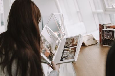 Rear view of woman reading book at home