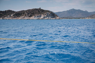 Scenic view of sea by mountain against sky