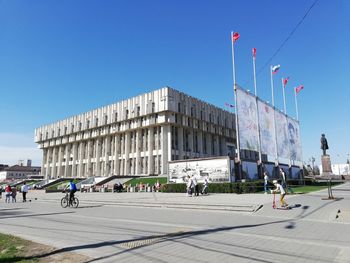 People walking in front of buildings against blue sky