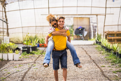 Portrait of teenage boy piggybacking mother in greenhouse