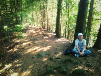 Woman sitting on pathway amidst trees in forest