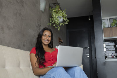 Young black woman working at home with laptop on her lap sitting on her couch  notebook for working. 