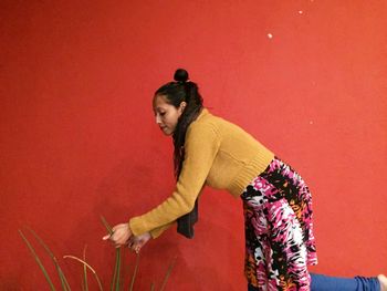 Woman cutting plant while standing against red wall