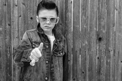 Portrait of boy holding sunglasses standing on wood