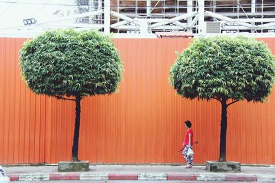 Side view of woman walking by orange corrugated iron on sidewalk