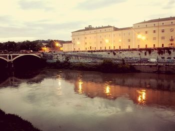 Bridge over river by illuminated buildings against sky