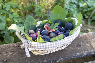 A wicker basket full of freshly picked purple figs on a wooden table. 