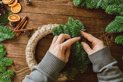 Top view of male hands making a christmas wreath from natural spruce branches and various decoration