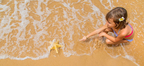 High angle view of girl pointing at starfish on seashore