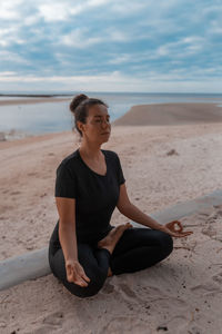 Portrait of young woman sitting at beach against sky