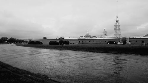 Helicopter at riverbank by church against cloudy sky