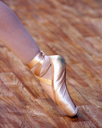 Low section of woman wearing ballet shoes on hardwood floor