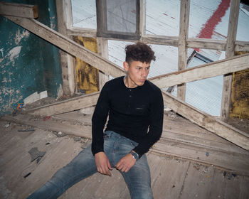 Young man looking away while standing on wood