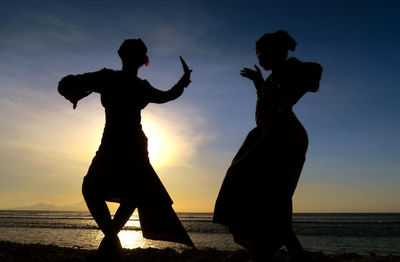 Silhouette women dancing at beach against sky