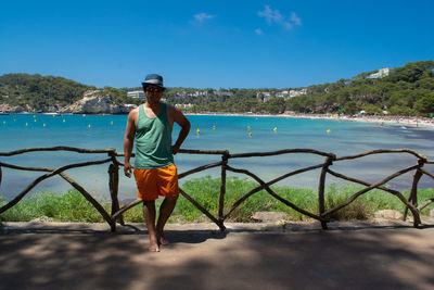 Full length of man standing at sea shore against blue sky