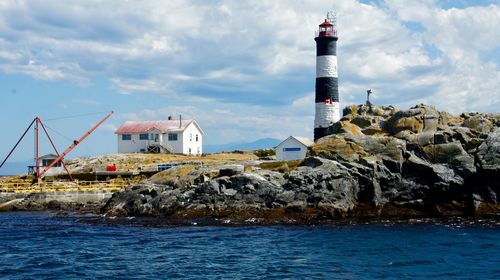 Lighthouse by sea against buildings