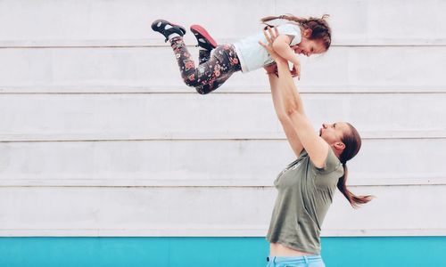 Side view of playful mother tossing daughter against white wall