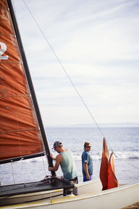 Man making sailboat while standing with father at beach