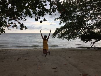 Portrait of woman jumping with arms raised at beach 