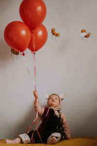 Toddler baby girl in funny hat with ears sitting with balloons