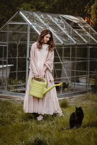 Pretty woman at her 30s in the garden with watering can and cat walking on the grass. beautiful