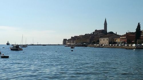 Sailboats in sea by buildings against sky