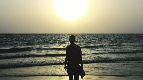 Silhouette of people standing on beach at sunset