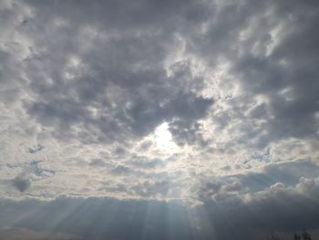 Low angle view of sunlight streaming through clouds