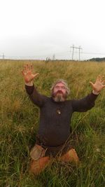 Portrait of young woman with arms raised on field against sky