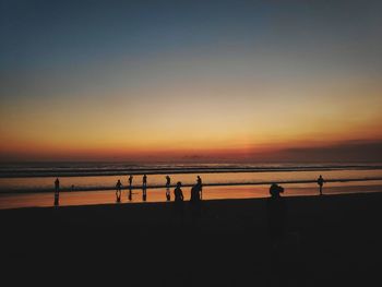 Silhouette people on beach against sky during sunset
