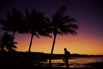 Silhouette man on palm trees at beach against sky during sunset