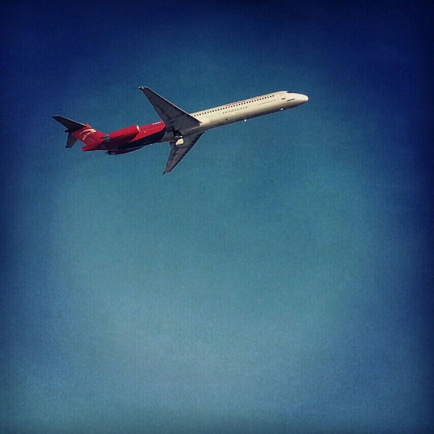 low angle view, flying, flag, patriotism, clear sky, identity, air vehicle, blue, national flag, airplane, transportation, copy space, mid-air, travel, sky, outdoors, american flag, wind, day, mode of transport