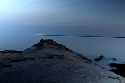 Rocks by sea against sky at dusk