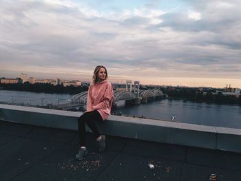 Full length portrait of young woman sitting against sky during sunset