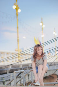 Happy young woman tying shoelace while standing on bridge at temple