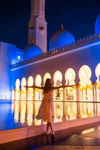 Rear view of woman standing against illuminated building