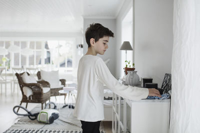 Side view of boy cleaning cabinet in living room