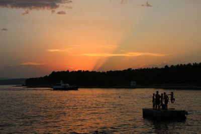 Silhouette people in sea against sky during sunset