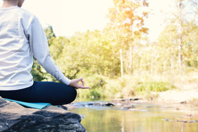 Midsection of woman doing yoga on rock by lake