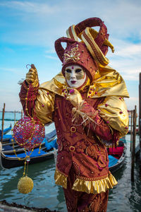 Man wearing venetian mask while standing by sea against sky