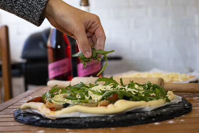 Hand throwing arugula to a vegetarian pizza.