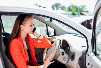 A young woman is sitting at the wheel of a car and talking on a mobile phone. transport management.